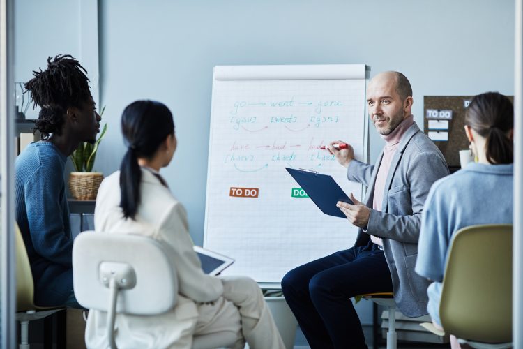 Portrait of smiling mature coach giving English lesson to group of people sitting in circle during seminar in office