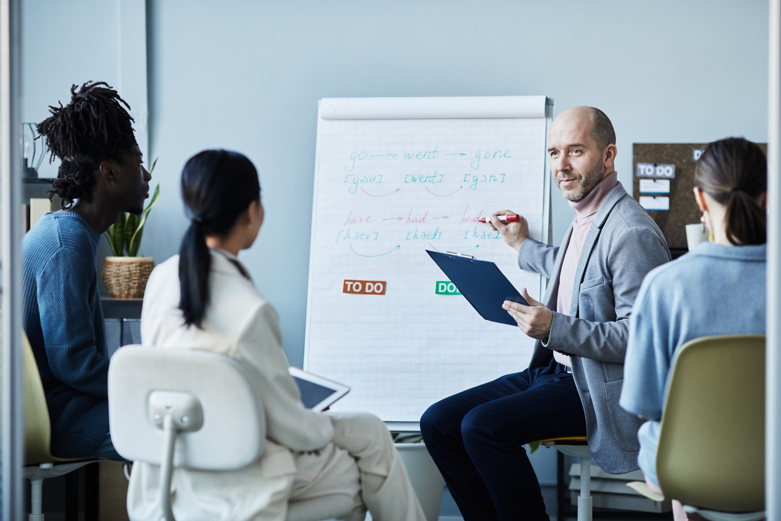 Portrait of smiling mature coach giving English lesson to group of people sitting in circle during seminar in office